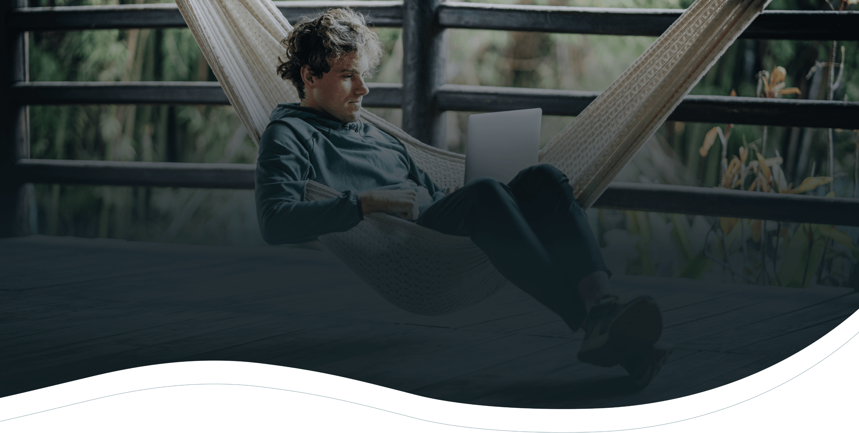 Man sitting on a hammock, working on his laptop on a balcony.